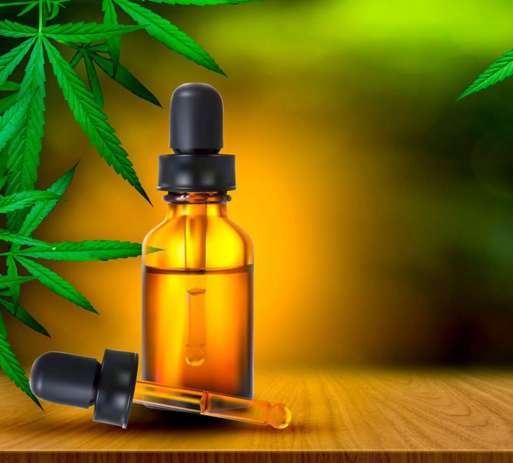 Amber glass dropper bottle with CBD oil, surrounded by green hemp leaves, on a wooden surface, highlighting natural remedies related to hemp and cannabis.