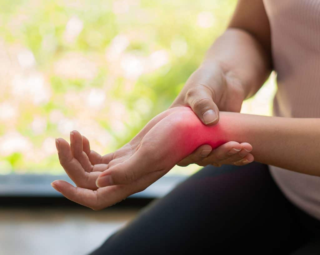 Person holding their wrist with visible redness, indicating inflammation, in a natural setting, relating to hemp's potential benefits for pain relief and inflammation management.